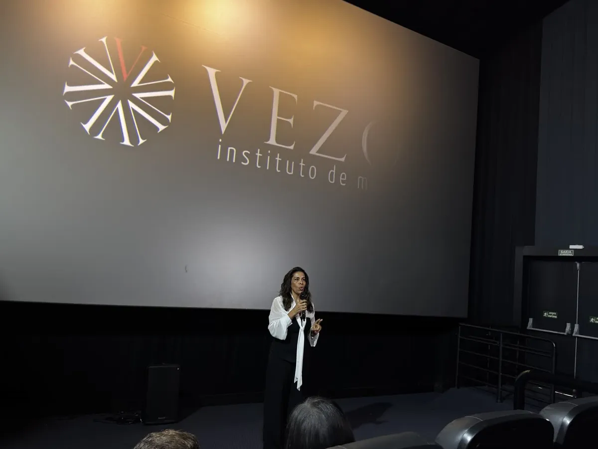 Fundadora do Vezo Instituto de Moda fala à plateia no cinema, com a marca projetada na tela